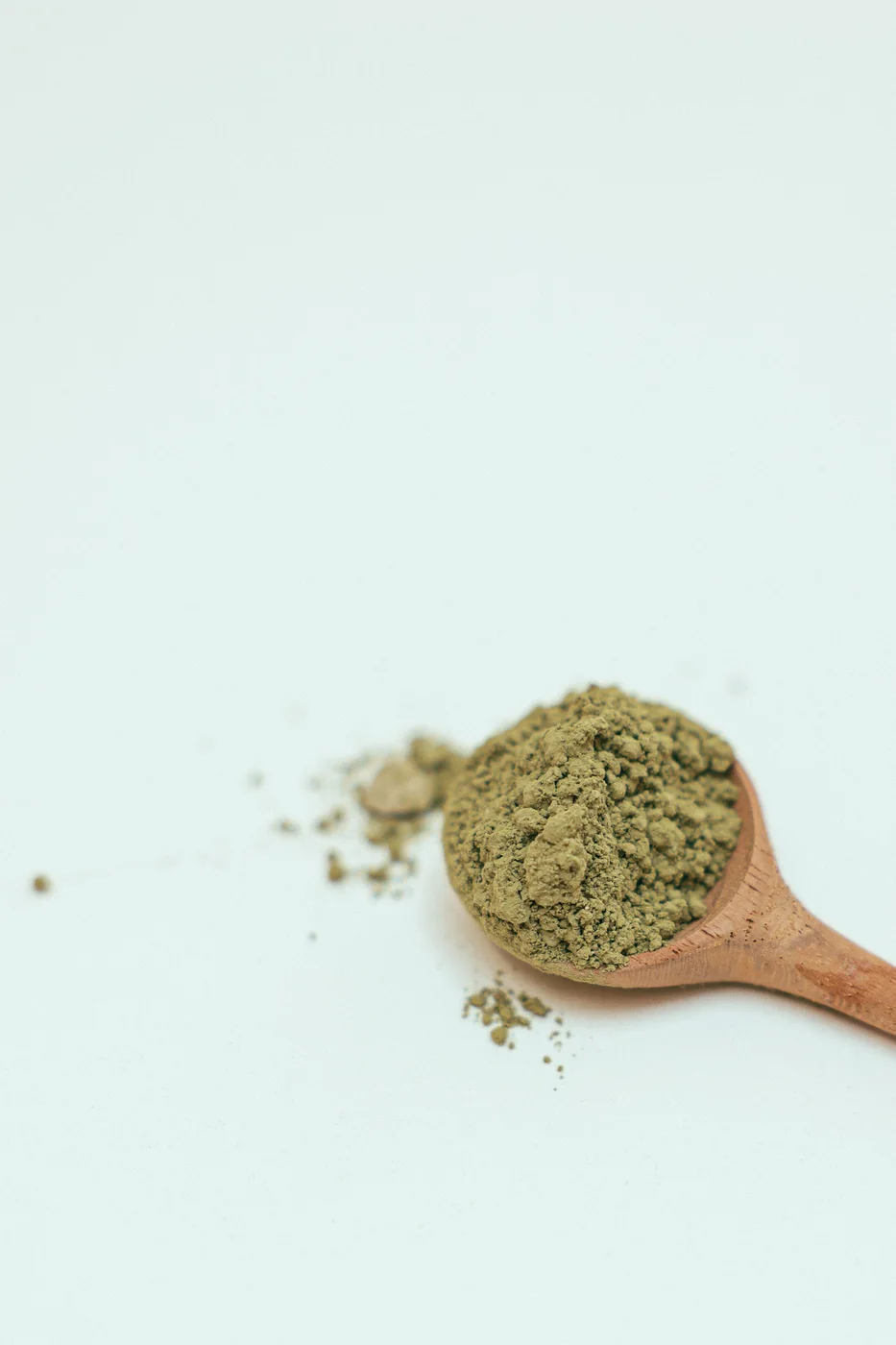 Powdered green tea extract heaped on a small wooden spoon on a pale surface