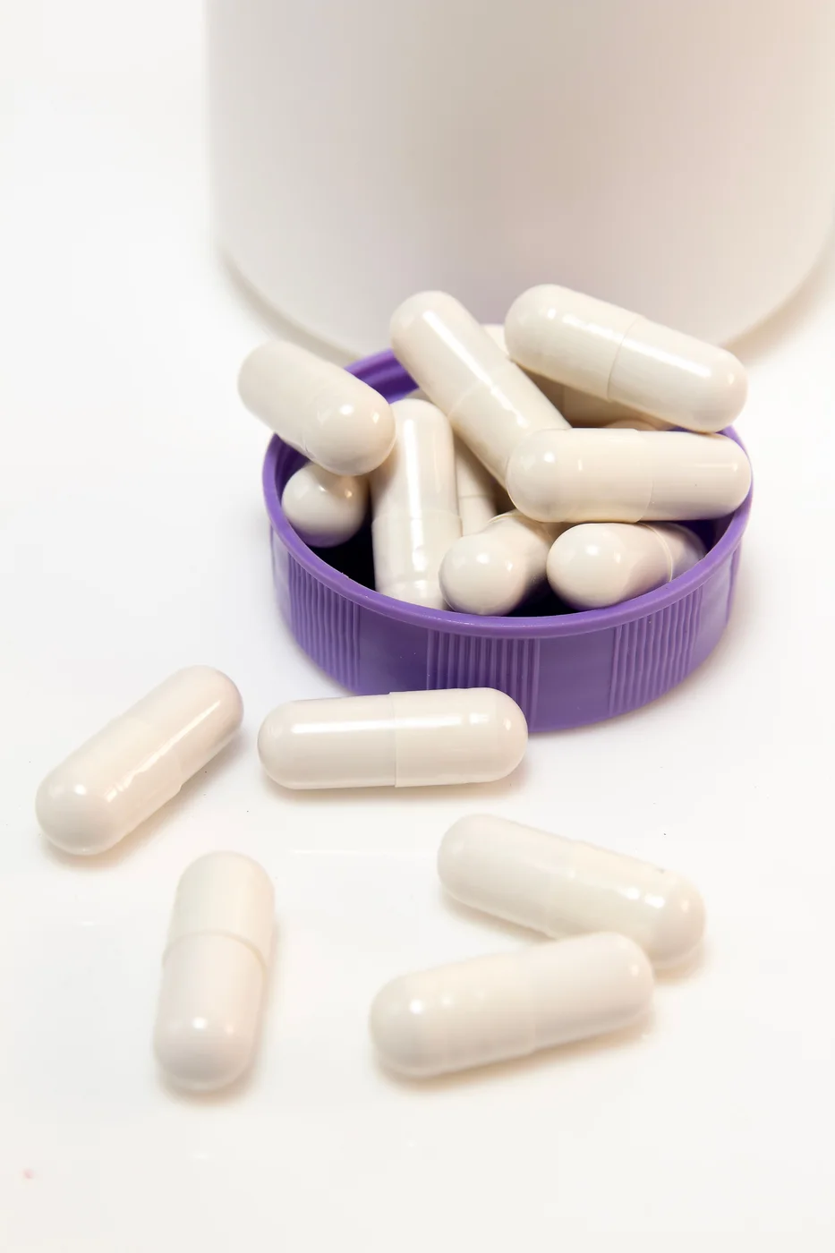 White L-arginine capsules tipped from a bottle onto a bright white surface