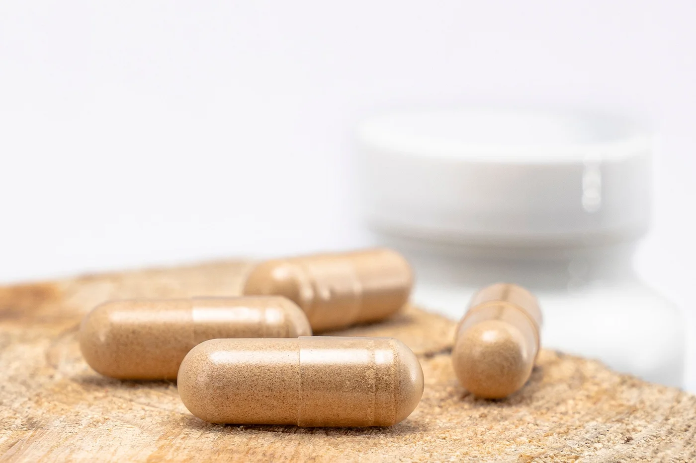 Pale maca root capsules spilling from a white jar onto fine sand